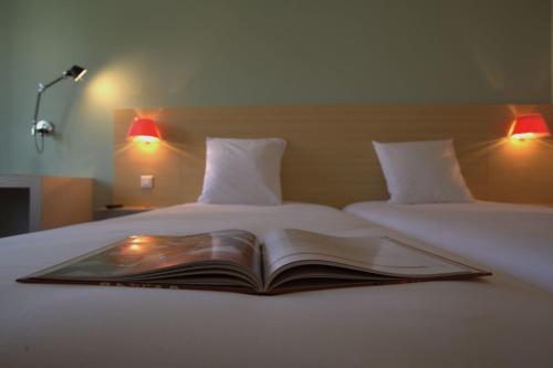 an open book on a bed with two lamps at ibis Styles Le Puy en Velay in Le Puy en Velay
