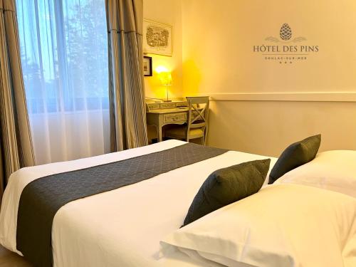 a hotel room with two beds and a desk at Hotel des Pins in Soulac-sur-Mer