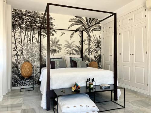 um quarto com uma cama de dossel e um mural de palmeiras. em VILLA DE LA LUZ Luxury Guesthouse em El Portil