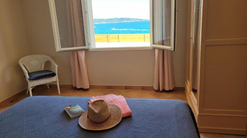 einen Hut auf einem Bett in einem Zimmer mit Fenster in der Unterkunft Villa en bord de mer face à l'Ile de Porquerolles in Hyères