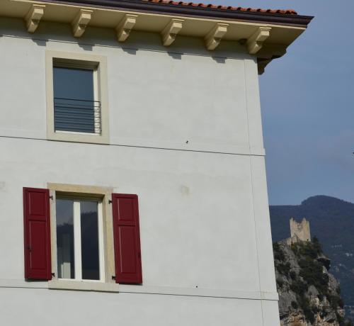 a white building with red windows and a castle in the background at Palazzo Oltre in Arco