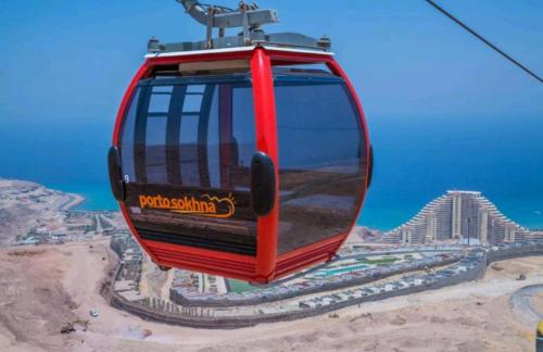 a red cable car flying over a city at شاليه فاخر بالبانوراما بورتوسخنه للعائلات فقط porto sokhna chalets in Ain Sokhna