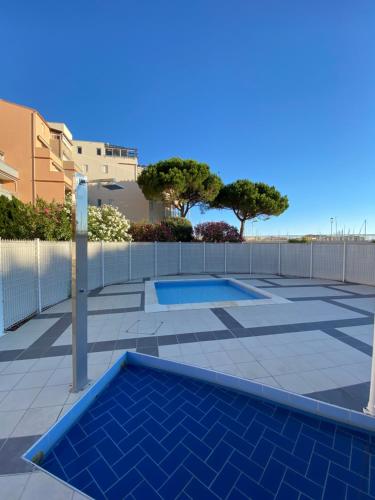 a swimming pool in a yard with a fence and trees at Studio Le Pharo Résidence avec piscine in Cap d'Agde