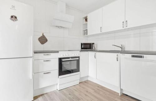 a white kitchen with white appliances and wooden floors at Lovely 1 bedroom downstairs condo with free parking place in Svolvær