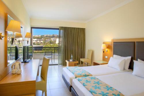 a hotel room with two beds and a desk and a balcony at Sol Cosmopolitan Rhodes in Ixia