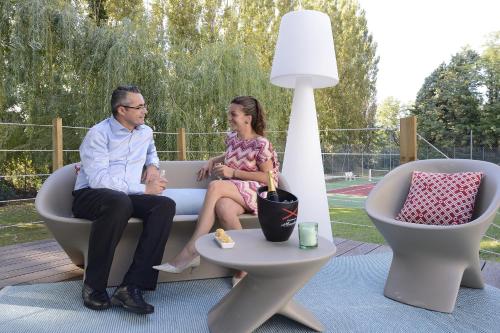 a man and a woman sitting on a couch in a patio at Novotel Avignon Nord in Sorgues