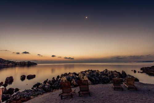 four chairs sitting on the shore of a body of water at Nobelos Seaside Lodge in Agios Nikolaos