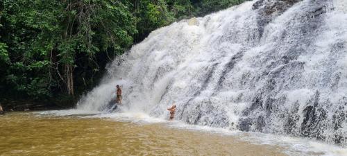 two people standing in the water in front of a waterfall at Aldeia Setemares Bangalôs - Praia do Sargi - Serra Grande in Serra Grande