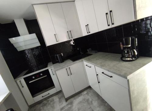 a kitchen with white cabinets and a black tile wall at Apartament Heaven in Ełk
