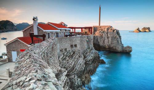 a building on a cliff next to the water at Vista Petrovac in Petrovac na Moru