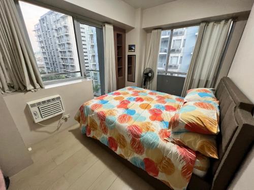 een slaapkamer met een bed met een kleurrijk dekbed en ramen bij Resorts World Condo in Manilla