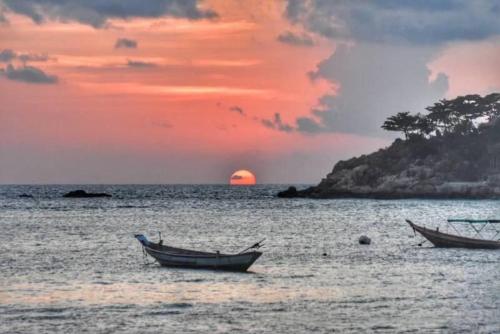 two boats in the water with a sunset in the background at Big Fish Resort Koh Tao in Koh Tao