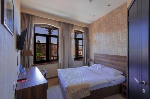 1 dormitorio con 1 cama, escritorio y 2 ventanas en Old Meidan Tbilisi By Urban Hotels, en Tiflis