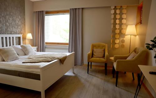 a bedroom with a bed and two chairs and a window at Hotel Kalevala in Kuhmo