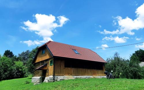 a wooden barn with a red roof on a green field at Bakina iža in Duga Resa