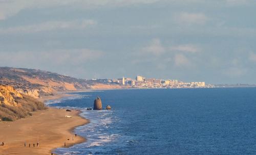 a beach with people standing on the sand and the ocean at La Casa de Oti playa Mazagón vistas al mar in Mazagón