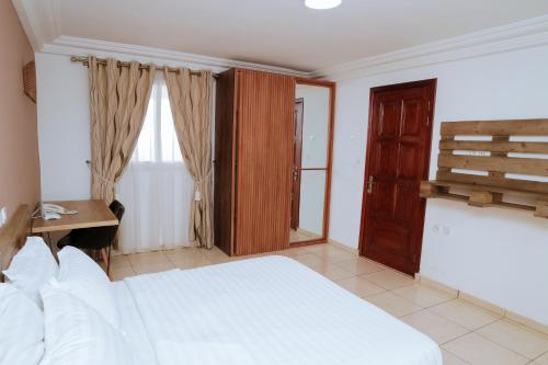 a bedroom with a bed and a desk and a window at RESIDENCE OLIE OFFICIEL in Douala
