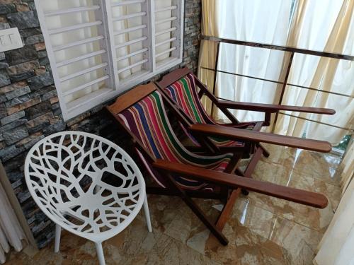 a wooden rocking chair and a white chair next to a window at CHILLAX Resorts Palakkayam THATTU in Paithalmala