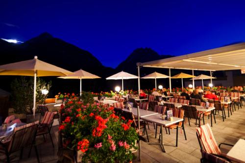 a restaurant with tables and chairs and flowers at night at Hotel Astras in Scuol