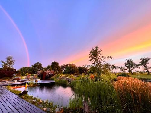 un arco iris en el cielo sobre un estanque con un puente en Wellness Hotel Boží oko, en Malé Chrášťany