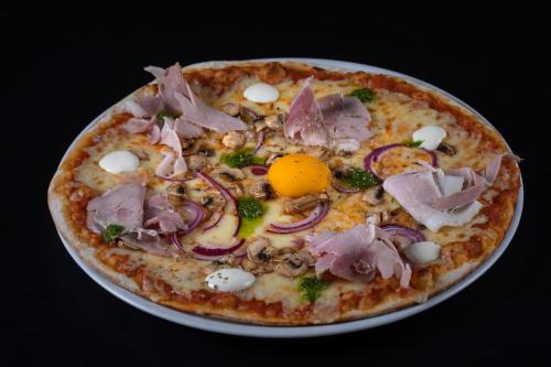 a pizza with ham and onions on a plate at Logis Hôtel Domaine du Moulin Cavier - Restaurants & Spa in Avrillé