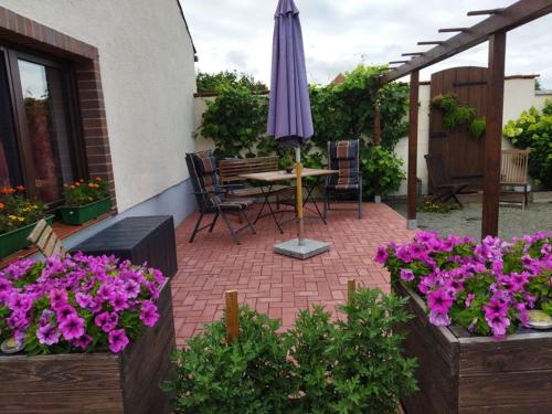 a patio with a table and umbrella and purple flowers at Ferienwohnung Familie Pohle in Lübbenau