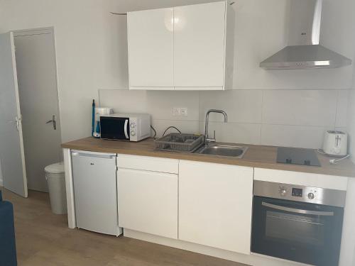 une cuisine avec des armoires blanches, un évier et un micro-ondes dans l'établissement La cigales, à Martigues