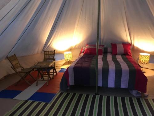 a bedroom with a bed and two chairs in a tent at LE PETIT REFUGE DU VAL D’EMERAUDE in Soudorgues