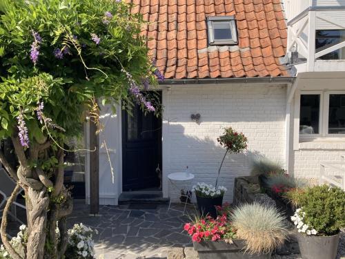 a white house with a black door and some flowers at LE CHALET de LA LONGERE in Beuvry-Nord