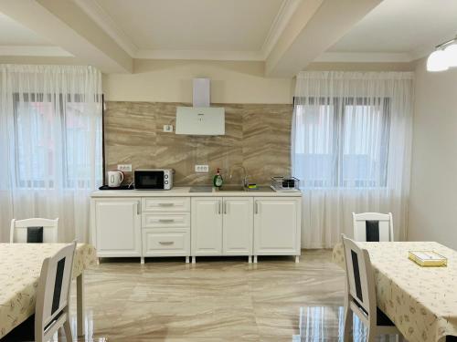 una cucina con armadi bianchi, tavoli e finestre di M House Băile Herculane a Băile Herculane