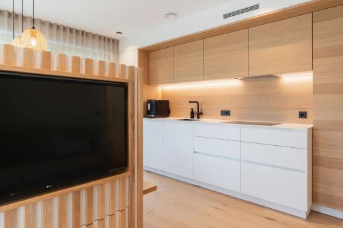 a kitchen with white cabinets and a flat screen tv at VANEA - Alp Relax Guesthouse in Chienes