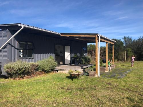a black house with a porch and a woman standing outside at Casetta del Fuoco - Eco Container Cottage in Plettenberg Bay