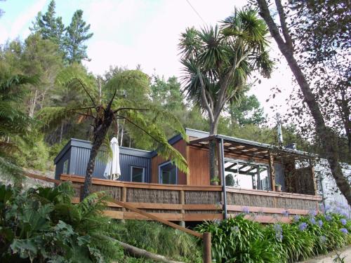 a house in the woods with a wrap around deck at Cabbage Tree Chalet in Parapara 