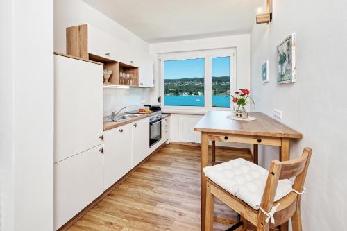 una cucina con armadi bianchi, tavolo e finestra di Appartements Schwarzvilla a Velden am Wörthersee