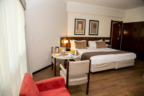 a bedroom with a bed and a table and a chair at Plaza Blumenau Hotel in Blumenau