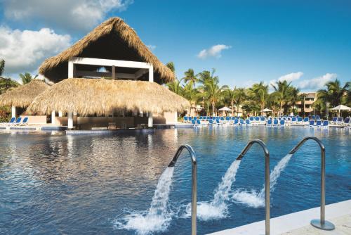 a swimming pool at a resort with a thatch roof at Royalton Splash Punta Cana, An Autograph Collection All-Inclusive Resort & Casino in Punta Cana