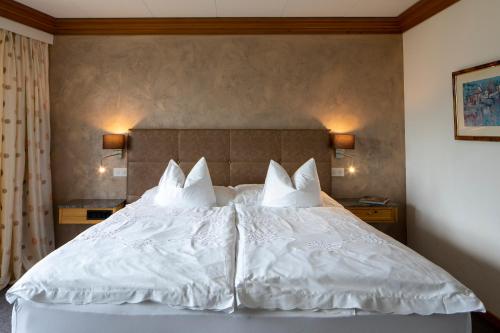 un letto con lenzuola e cuscini bianchi di Cristallo Arosa Hotel a Arosa