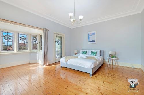 a white bedroom with a bed and a wooden floor at KOZYGURU Campsie Oldie-but-goodie look 4 Bed House NCA011 in Sydney
