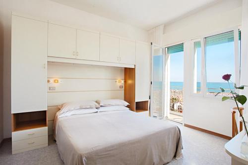 a white bedroom with a bed and a large window at Hotel Miramare in Caorle