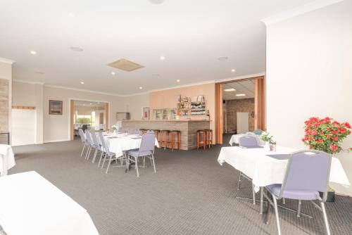 un comedor con mesas blancas y sillas blancas en Seasonal South Motel & Function Centre, en Ulverstone