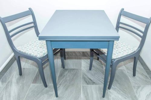 2 Stühle und ein blauer Tisch sowie ein Tisch und Stühle in der Unterkunft BB Apartman Hajdúnánás in Hajdúnánás