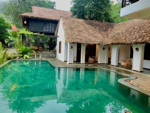 a villa with a swimming pool and a thatch roof at Mai Chau Rustic Home in Mai Chau