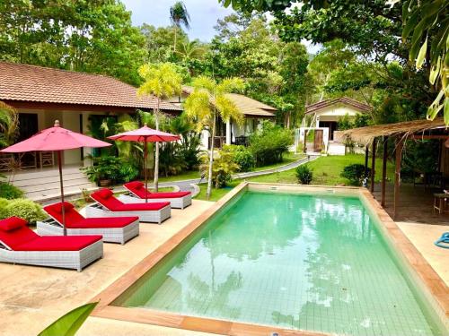 a pool with chairs and umbrellas next to a house at Carpe Diem Residence in Thongsala