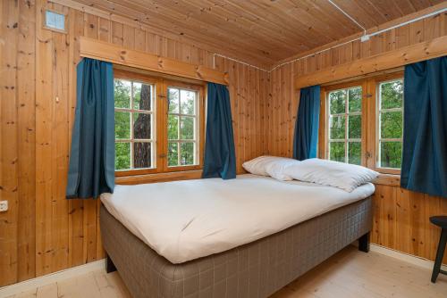 a bed in a room with wooden walls and windows at Ljoshaugen Camping in Dombås