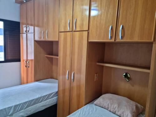 um pequeno quarto com 2 camas e armários de madeira em Apartamento aconchegante a 100m da praia na Praia Grande