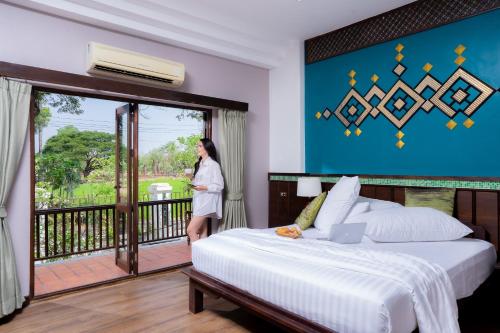a woman standing in front of a bed in a hotel room at Legendha Sukhothai Hotel - SHA certified in Sukhothai