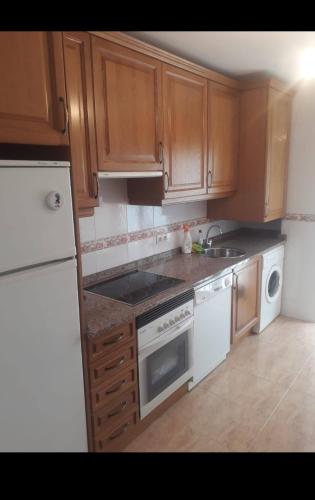 a kitchen with wooden cabinets and a white refrigerator at Apartamento cerca de playas in Soto del Barco