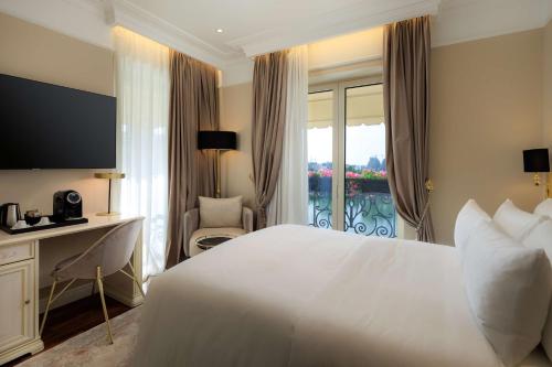 a bedroom with a white bed and a desk and a window at Radisson Collection Morina Hotel, Tirana in Tirana