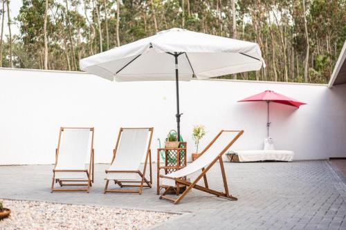 three chairs and an umbrella on a patio at Quinta do Vale Vendeiro in Figueira da Foz