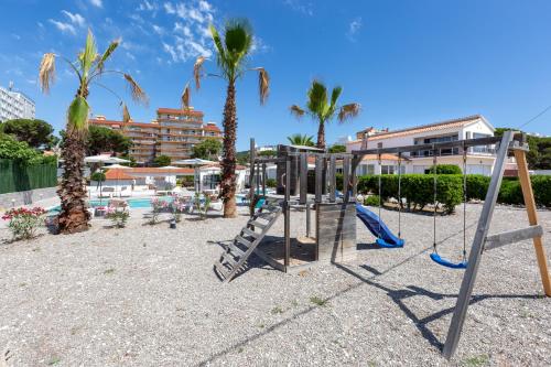 un parque infantil con columpios y palmeras en Malgrat de Mar Beachfront Village, en Malgrat de Mar